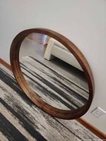 Full view of round mirror leaning against wall, showing woodgrain frame and reflection