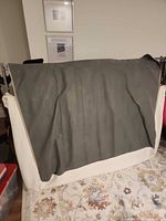 Folded metal box spring covered by grey fabric panel resting on white zip cover