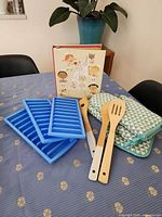 Overall lot showing cookbook, three ice cube trays, three utensils, quilted mitts and pot holder