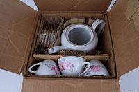 Open box showing packed teapot, cups, saucers with cardboard dividers