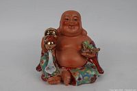 Front view of multicolour porcelain laughing Buddha holding gold orb and ingot