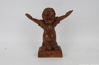 Front view of carved wood figurine showing outstretched arms and inscription