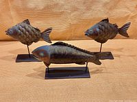 Three hammered metal fish figures on stands