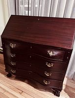 Front view of closed desk showing slanted lid, four serpentine drawers, brass hardware, ball-and-claw feet