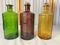 Front view of three colored octagonal bottles showing size, color and corks