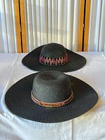 Two black straw floppy hats side by side showing bands and brim size