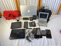 Overview of all electronics on table including Apple MacBook, Dell laptop, iPad, smartphones, tablets, portable DVD, action camera, cables, red pouch