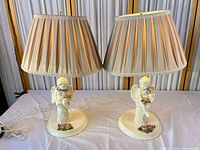 Both porcelain cherub lamps with shades displayed side by side