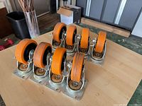 Eight orange rubber swivel casters with top plates and brakes arranged on tabletop