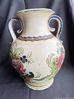 Full front view of cream Majolica-style vase with two handles and raised floral motifs
