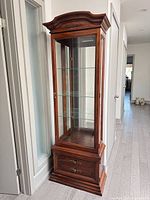 Full front view of curio cabinet closed showing crown, glass door, lower compartment