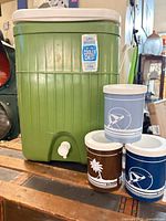 Front view of green cooler with spigot and three insulated cups
