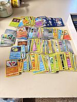 Overall view of multiple piles of Pokémon cards spread on table showing variety of colors and borders