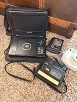 Group shot of all electronics: Audiovox DVD player, Kodak Disc camera, Fujifilm Instax camera, Aiwa cassette player