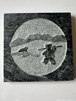 Full view of square soapstone plaque with circular carved scene and signature