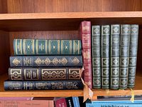 Shelf view showing all nine leather bound books including five uniform green Dickens volumes and four assorted titles