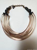 Full view of necklace showing five lucite strands, ribbon knots, brass extender chain with GA tag