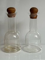 Both clear glass carafes with teak stoppers side by side
