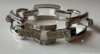 Full view of silver-tone bracelet showing links, rhinestones, green glass accents