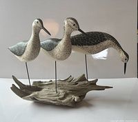 Full view of three carved shorebirds on driftwood base