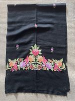 Full view of black wool shawl folded, showing main embroidered design