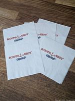Five white paper napkins with Scoops Ahoy and Chips Ahoy printing laid out on wooden surface