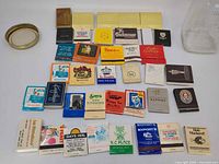 Top view of arranged matchbooks showing variety of advertising designs and two jar components