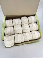 Open box displaying 12 balls of white crochet thread