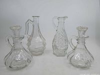 Group shot of four clear pressed glass cruets with stoppers