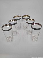 Six clear glasses with gold rims arranged in V shape