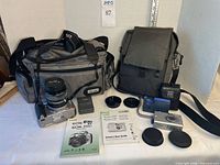 Overall lot view showing both cameras, charger, manuals, lens caps, and two camera bags