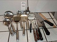 Overall view of 14 stainless, wooden and plastic kitchen utensils on tile surface