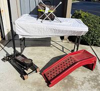 Black Craftsman floor jack, red ramp, cross lug wrench atop roadside kit on table