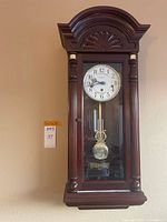 Front view of Howard Miller mahogany regulator wall clock hanging on wall