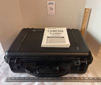 Closed hard carrying case with user manual on lid; measuring rulers for scale