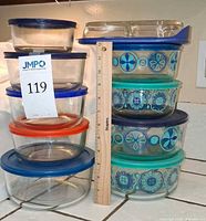 Stacks of clear and decorated Pyrex containers with lids, showing quantity and sizes