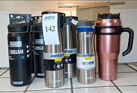 All eight stainless steel bottles and travel mug grouped on tiled surface with box behind