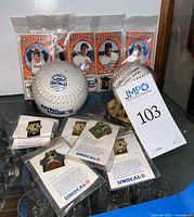 Group shot showing all items including packaged pins, Rawlings baseball in stand, DeBeer softball