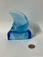 Front view of blue glass crescent moon tealight holder next to penny for scale