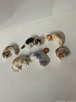 All six ceramic cat figurines arranged around coin for scale