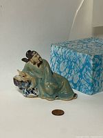 Front view of seated Shiwan Mudman figurine with box and scale coin