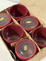 Six red paper maché glass votive holders inside divided cardboard box