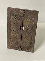 Angled view of closed carved wood frame showing hinged shutters and carved motifs