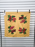 Full view of yellow tablecloth hanging showing four embroidered fruit clusters