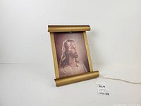 Front view of illuminated lithograph in scroll-style metal frame with power cord visible