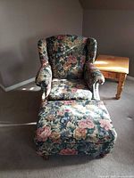 Front view of armchair with ottoman, showing floral upholstery and wooden feet