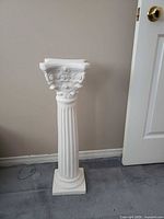 Full view of white ceramic column pedestal stand against wall