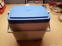 Front view of white Coleman cooler with blue lid and swing handle