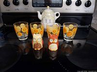 Front view: four orange-print glasses, teapot/mug set, two owl shakers