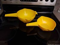 Top view of both yellow Tupperware strainers showing size difference and perforated interiors
